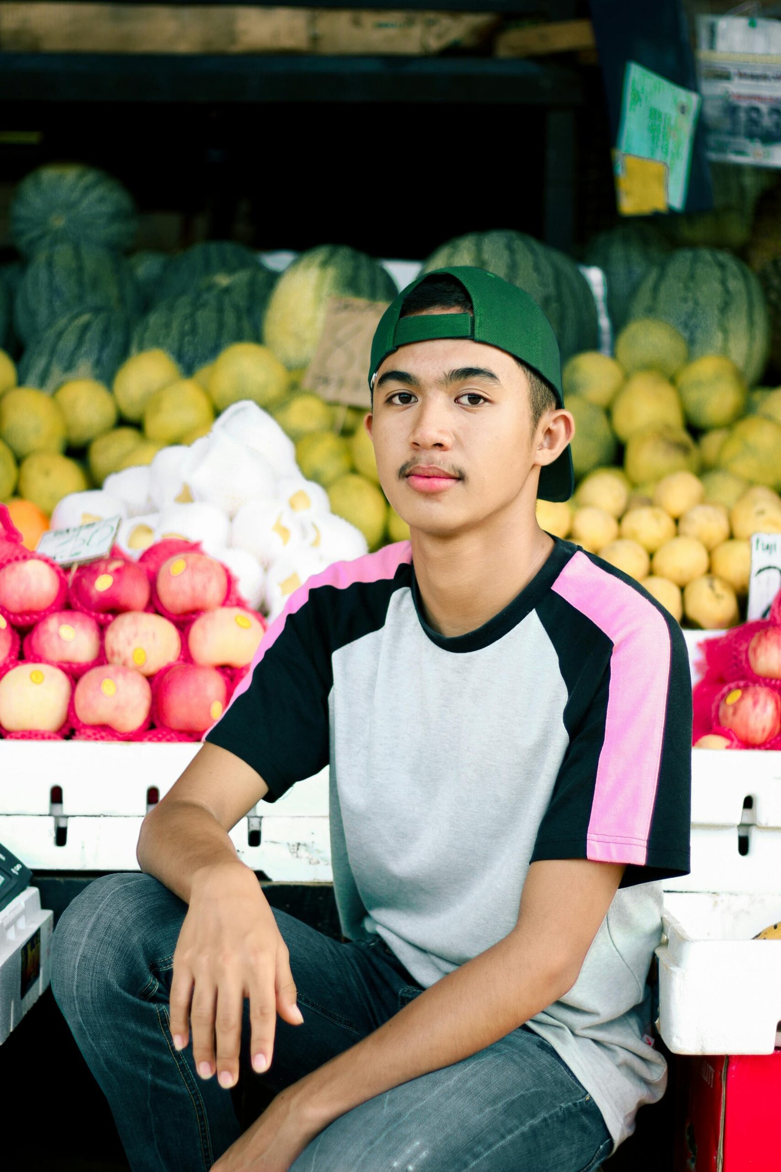 Joven, con camisa blanca y emprendimiento de frutas y verduras detras de el.