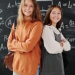 Dos Adolescentes felices frente a pizarrón, con las manos curzadas en espacios de aprendizaje de la comunidad crealib