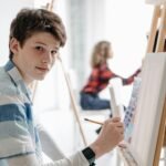 acdolescente aprendiendo en clases de dibujo Crealib, frente a un caballete mirando hacia la cámara feliz